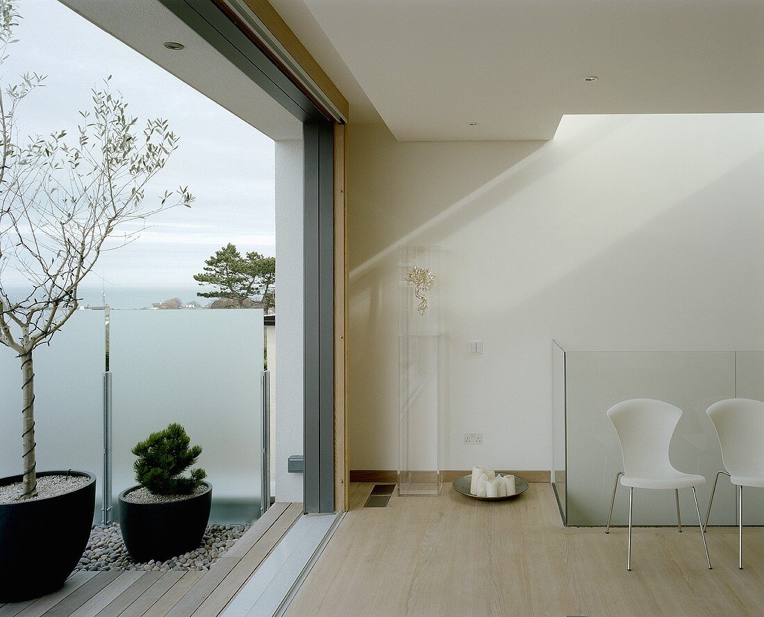 A modern living room with an open terrace door and a view of a terrace with wooden floorboards and potted plants