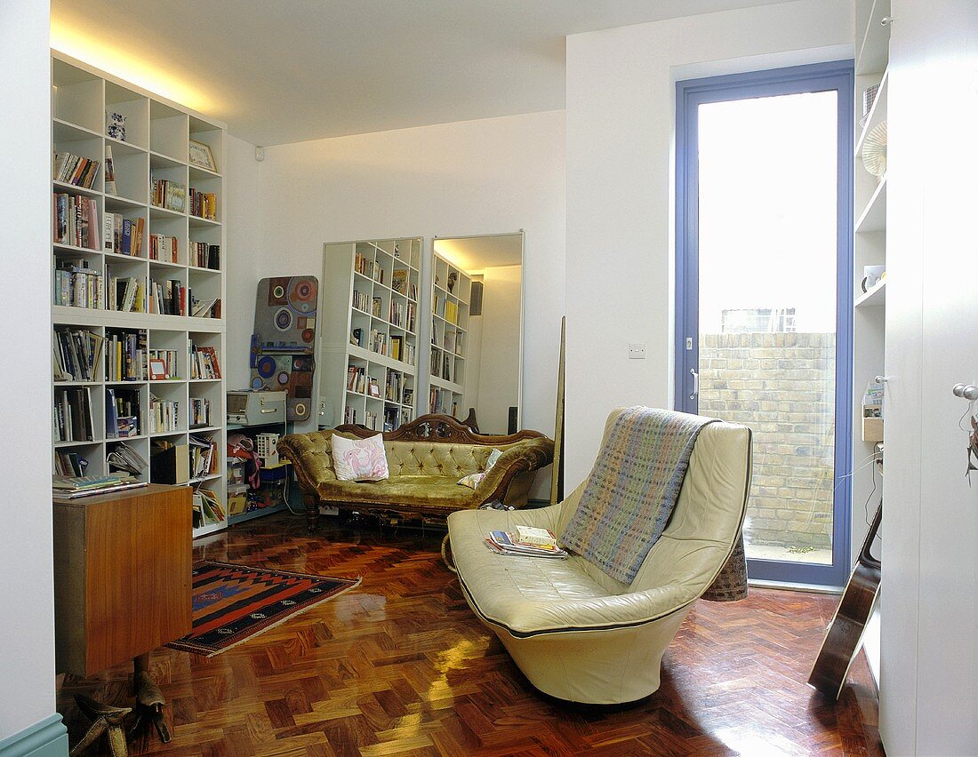 A living room with herring-bone parquet and a white leather sofa in front of terrace door and bookshelves with indirect lighting