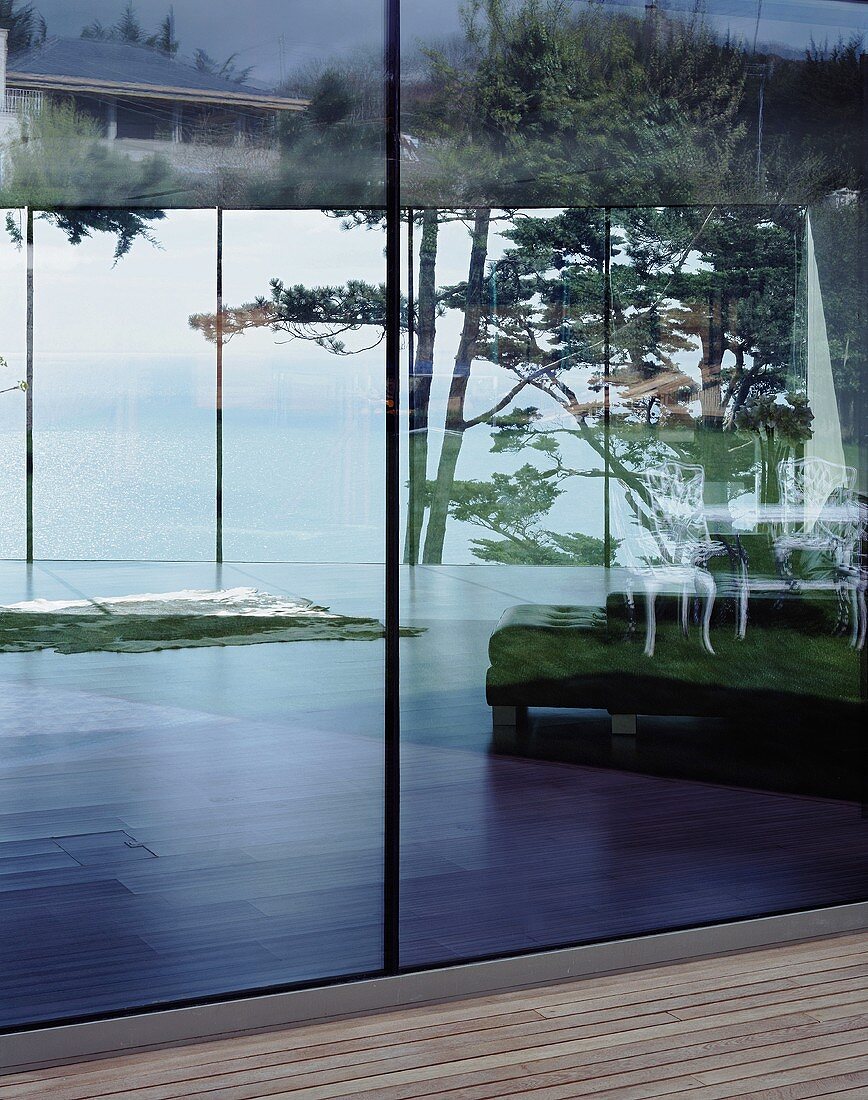 Terrassenausschnitt mit Holzdielen vor Glasfront und Landschaftsspiegelungen