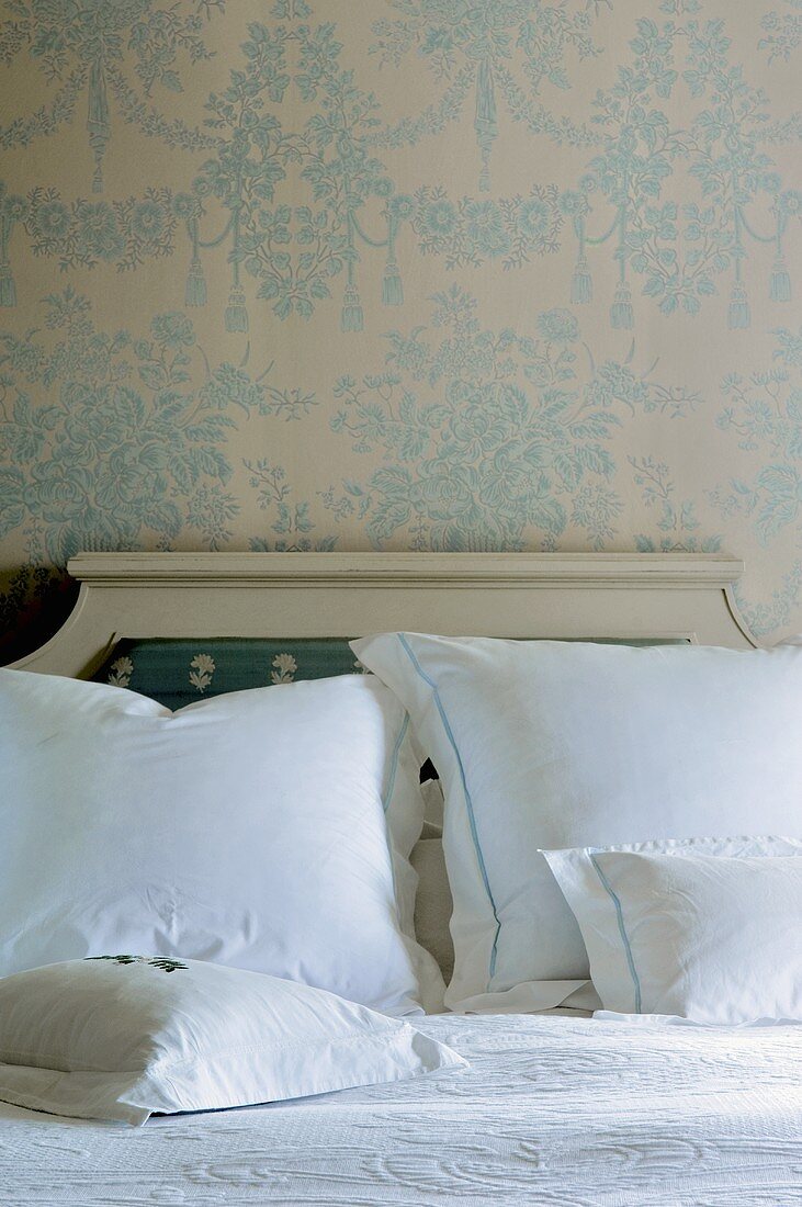 Englisches Doppelbett mit weissen Kissen vor zarter Tapete mit floralem Muster