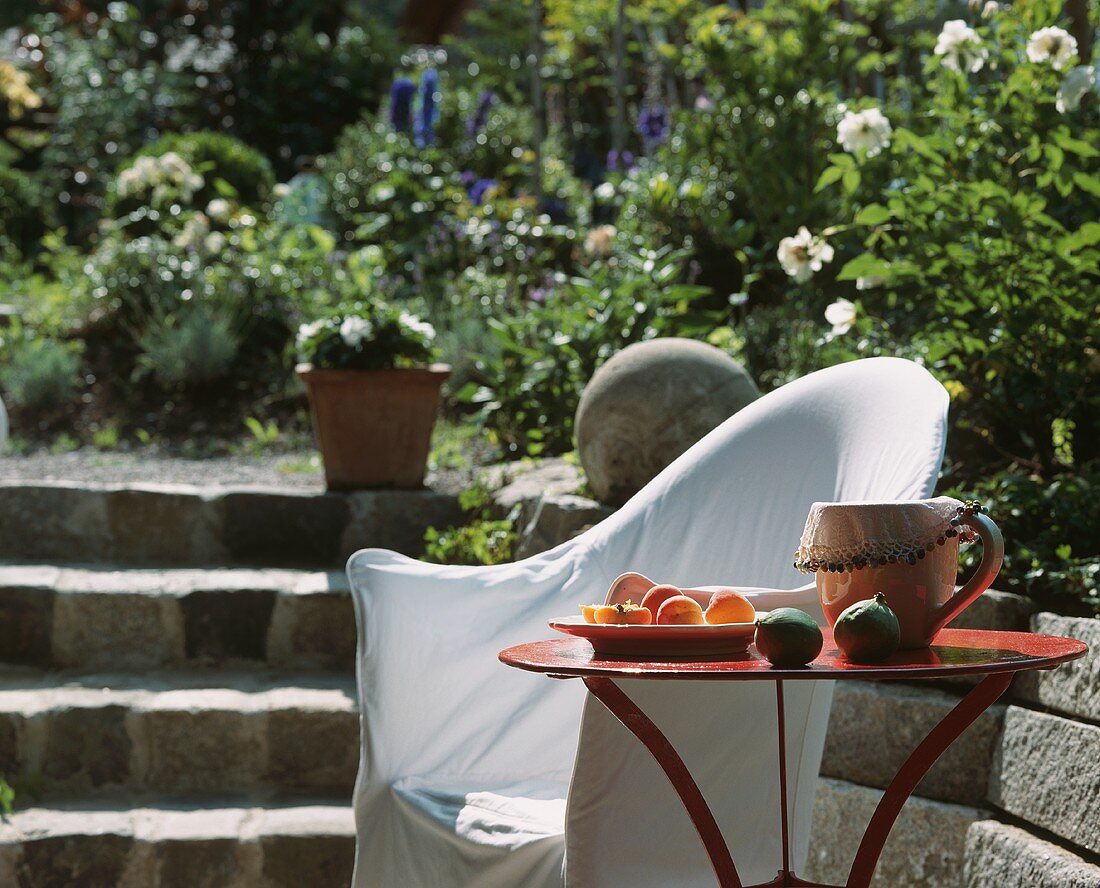Tisch und Stuhl mit weisser Husse an einer Treppe im blühenden Garten