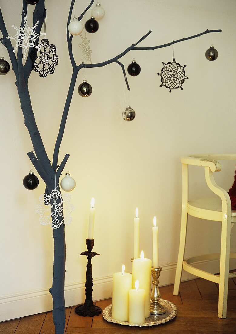 Weihnachtlich dekorierter Ast neben Silbertablett mit Kerzen