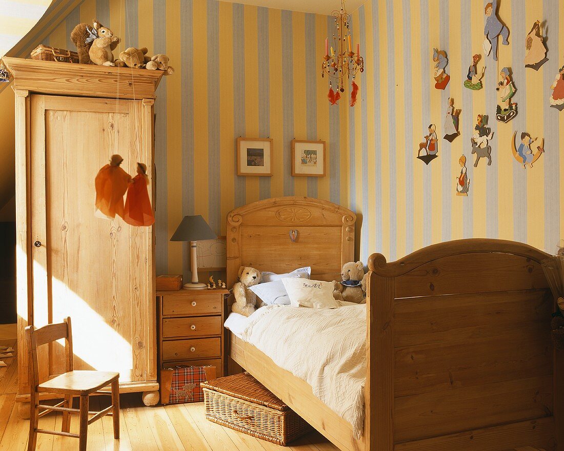 Kinderzimmer mit antiken Holzmöbeln und gelb und grau gestreifter Tapete; lustige Holzfiguren zieren eine Wand