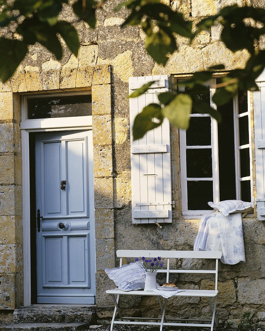 Altes, traditionelles Haus mit großem Sprossenfenster und Fensterläden; darunter eine kleine Sitzbank neben der Haustür