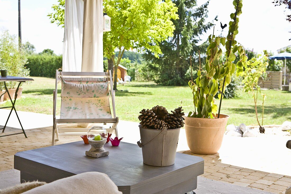 Gefüllter Eimer mit Pinienzapfen auf dem Terrassentisch mit Blick auf den Garten