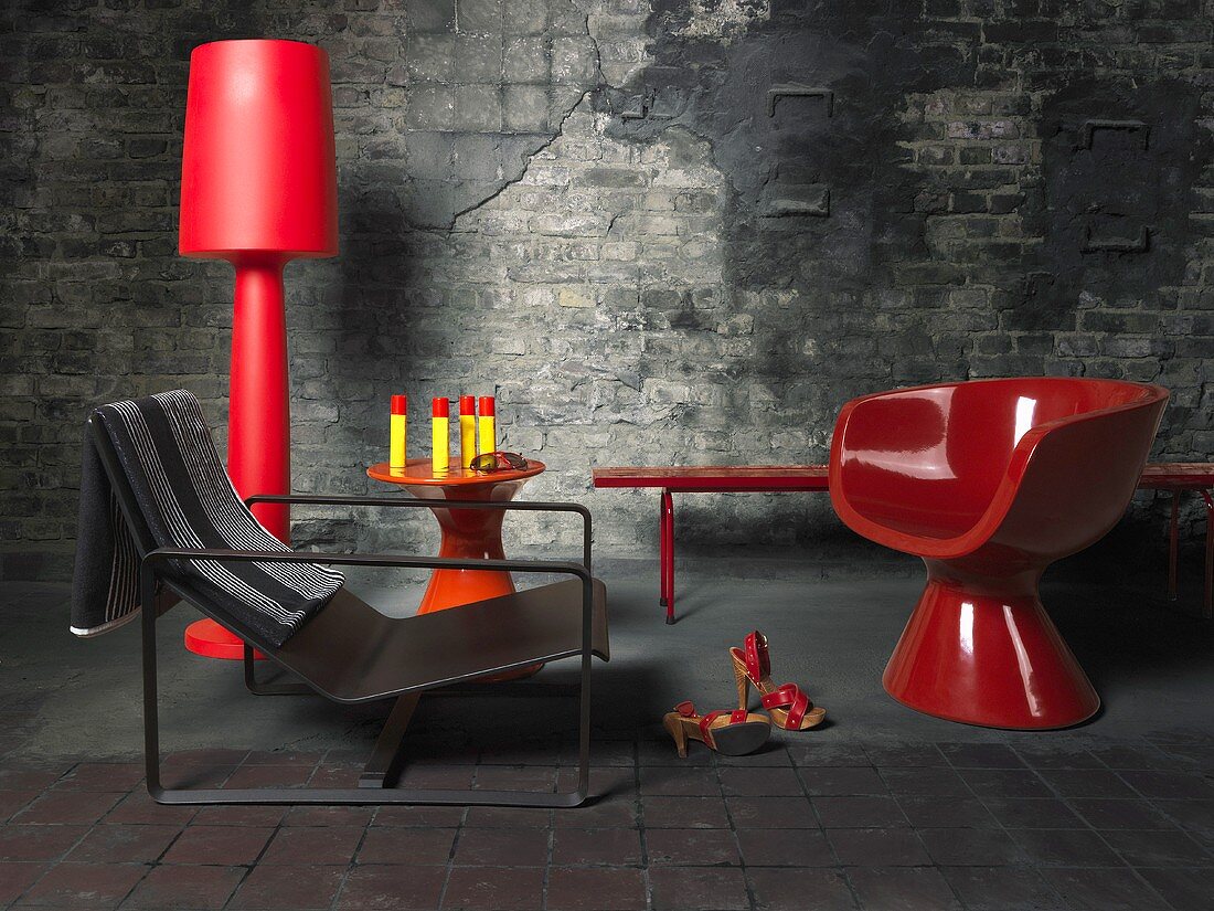 Moderne Möbel und Wohnaccessoires in Rot und Schwarz vor grauer, verwitterten Ziegelsteinwand