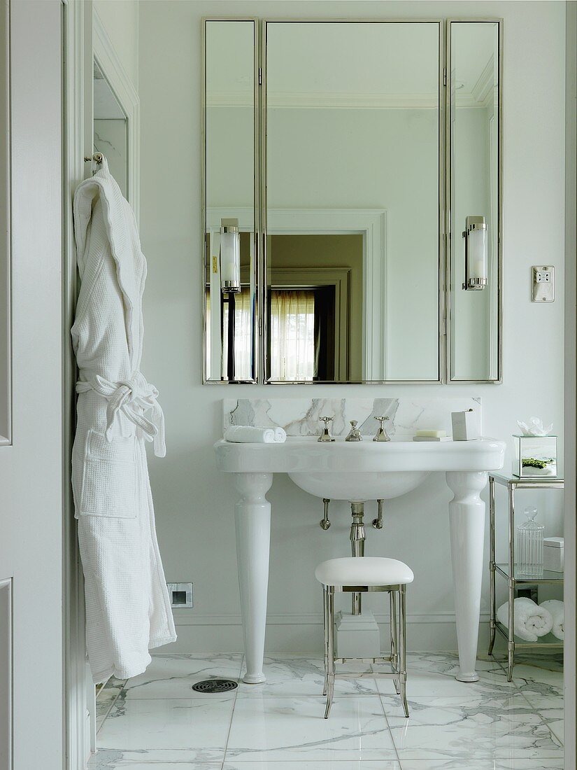 A built in mirrored cupboard in a white bathroom with a marble floor