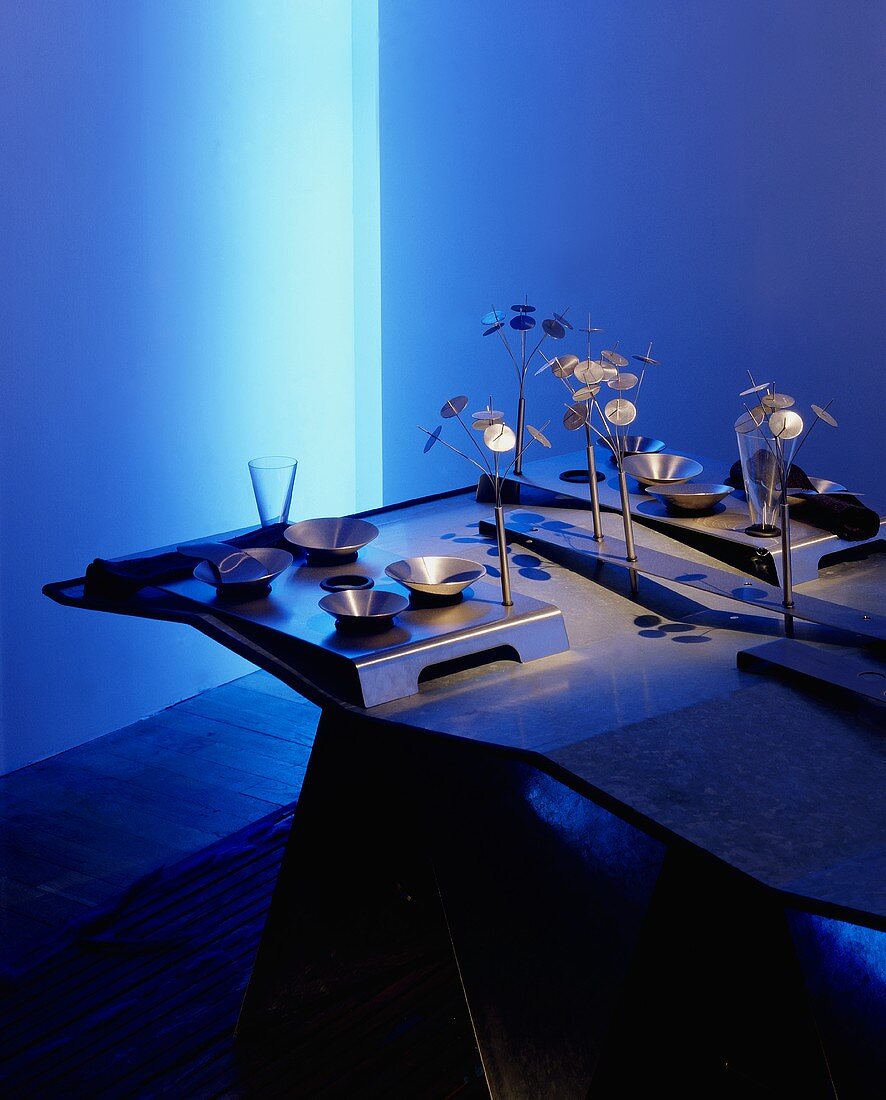 Metallgeschirr & moderne Deko-Objekte aus Metall auf blau beleuchtetem Esstisch