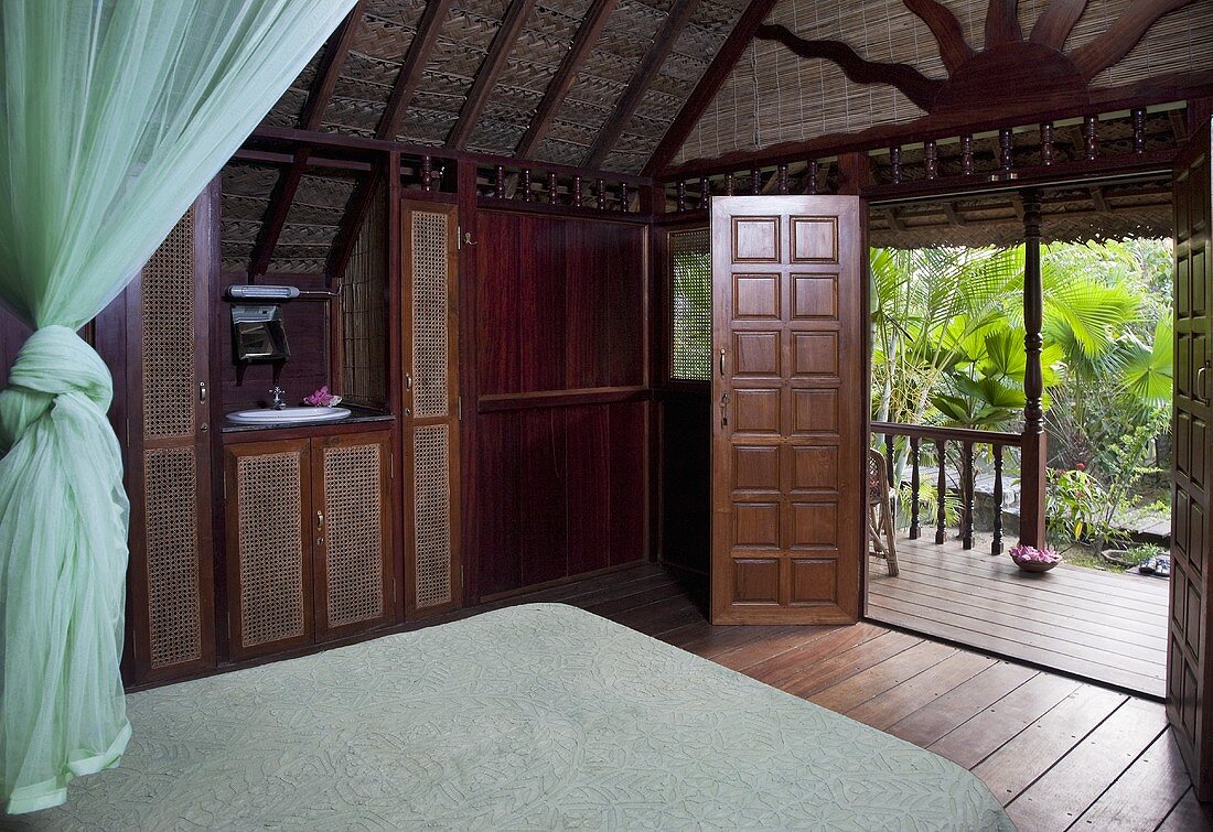 A wood panelled bedroom with view of a terrace and palm trees