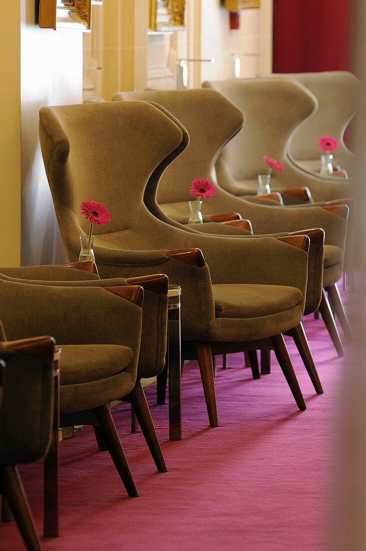 A row of winged armchairs with flowers on the side tables