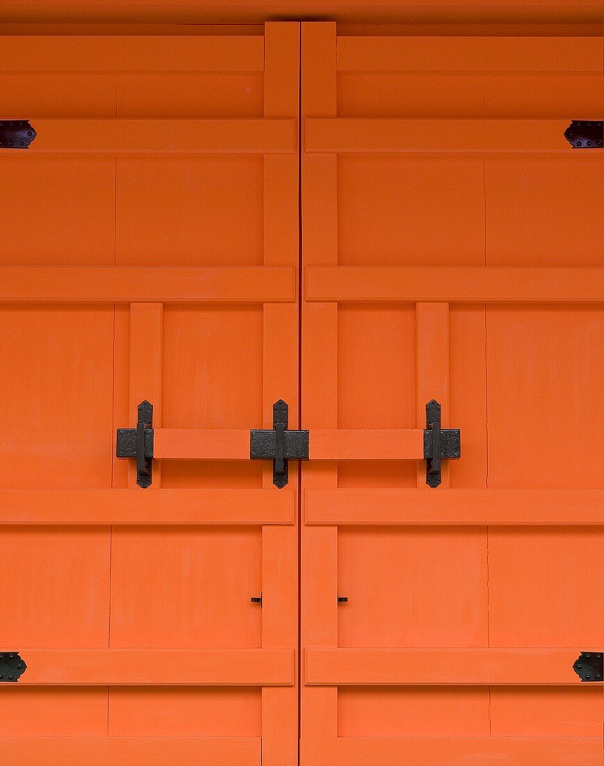 Detail of an orange-painted entrance door with a wrought iron bolt