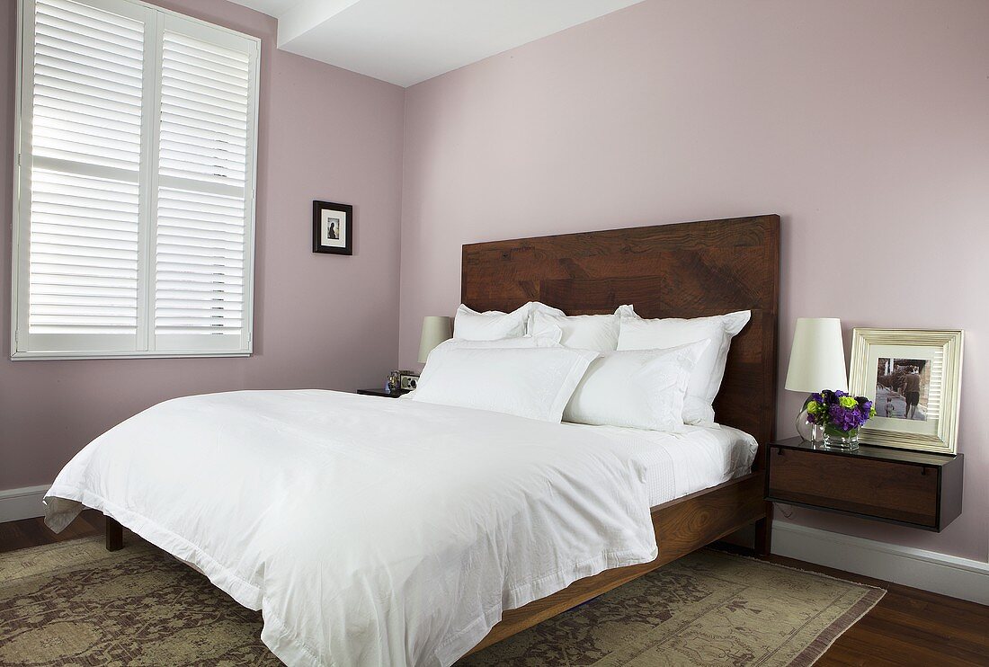 Schlafraum mit Doppelbett, hochgezogenem Kopfteil in Holzausführung & Nachtkonsole vor pastellrosa gefärbter Wand