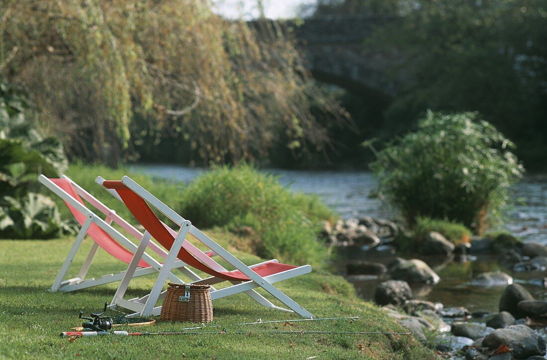Zwei Liegestühle und Angelruten an einem Fluss
