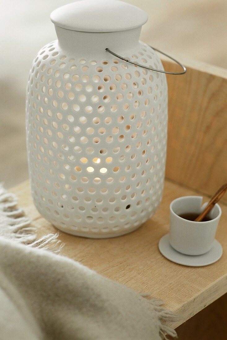 A white ceramic lantern with a cup of tea next to it