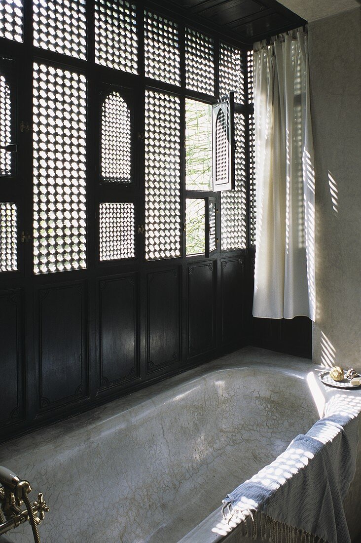 A Moroccan bathroom with a bathtub and wooden windows