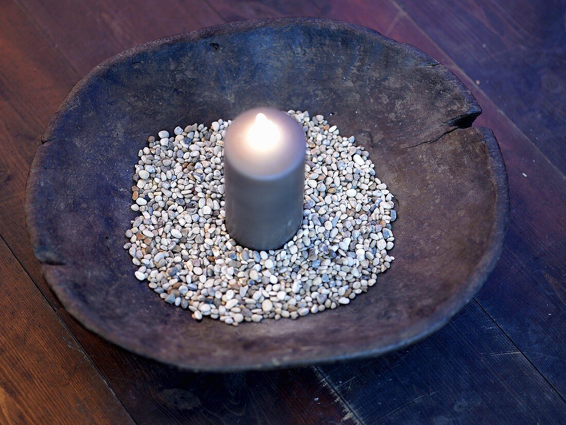 Lighted candle and decorative stones in a rustic wooden bowl