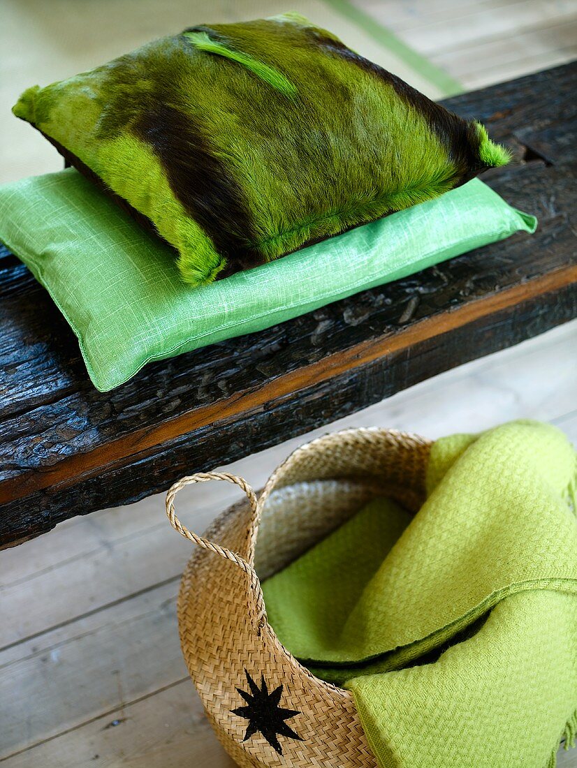Green pillows with a pelt cover on wooden planks and basket with a coverlet