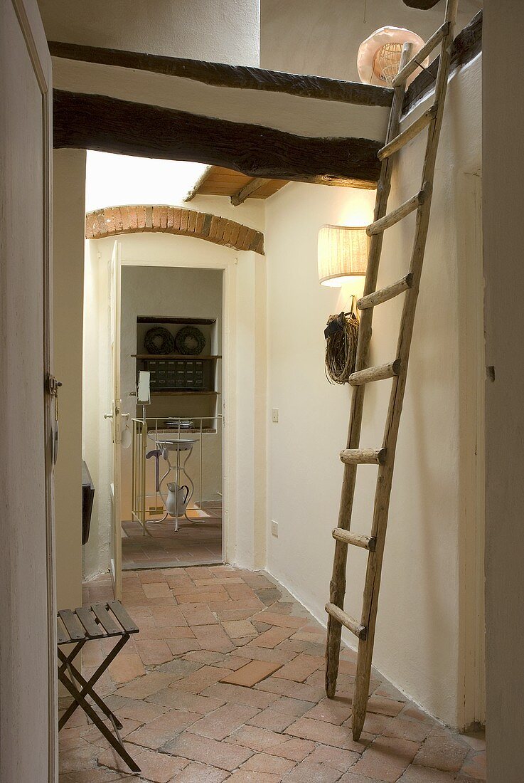 Holzleiter auf Terrakottafliesen im Dachgeschossflur mit Blick auf offene Tür