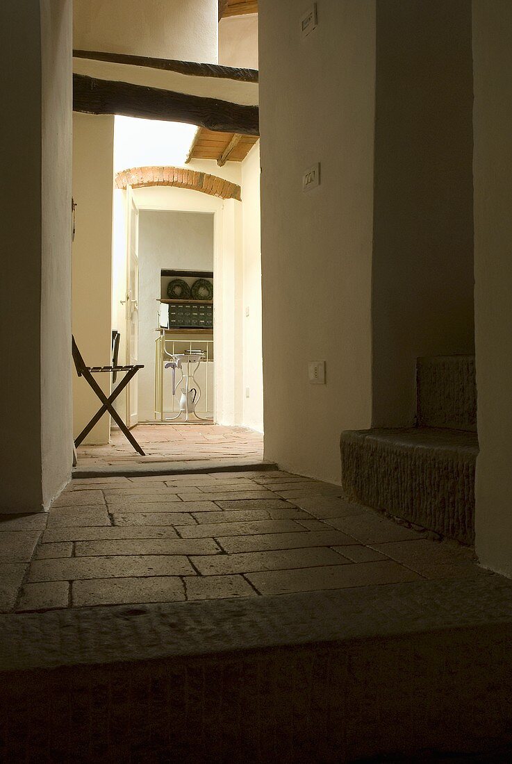 Stool in the entryway of a country home with terracotta tile and a view through an open door
