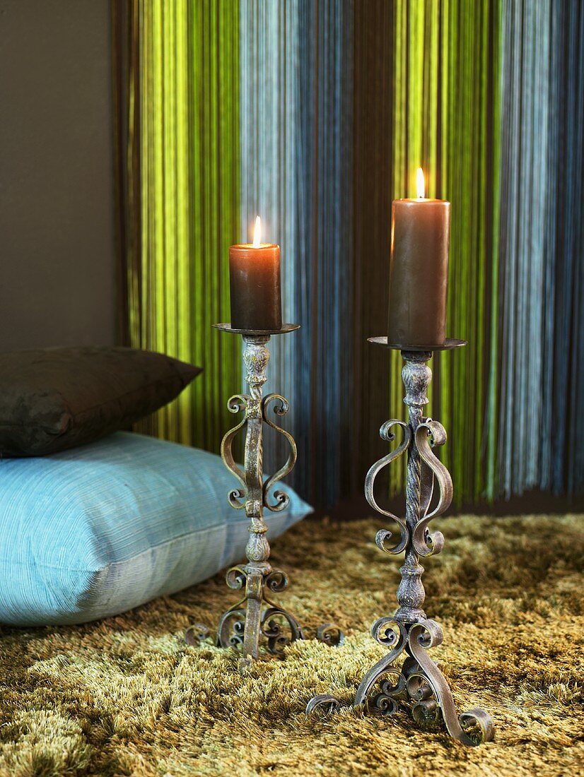 Antique metal candle holders with burning candles and pillows on a flokati rug