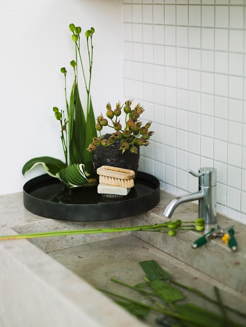Stone sink in front of white tiles with a black tray and flowers