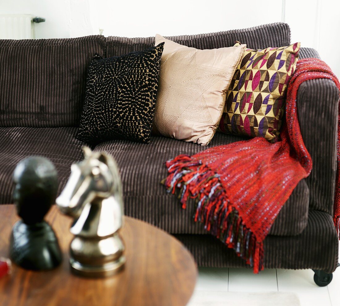 Brown corduroy sofa with pillows and a red throw