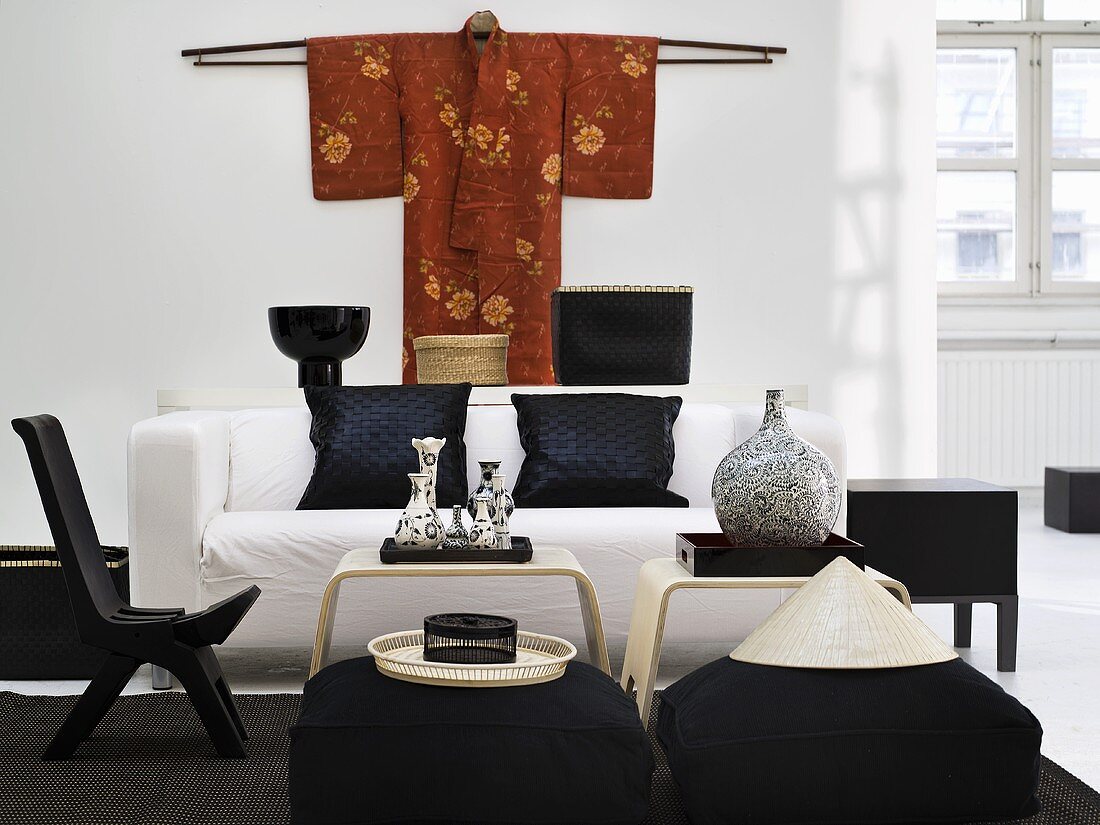 Schwarzer Stuhl und Sitzpolster mit weißem Sofa um Beistelltisch und gehängtem Kimono an Wand