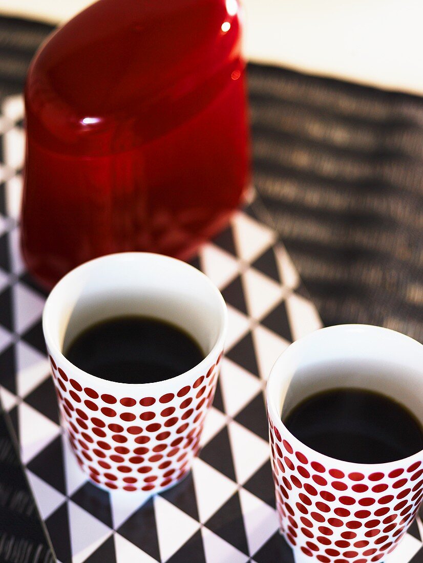 Filled coffee mugs and a red tin on a black and white surface