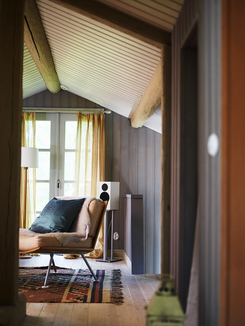Blick durch offene Tür in holzverkleidetem Dachraum eines Landhauses auf Sessel und Fenstertür