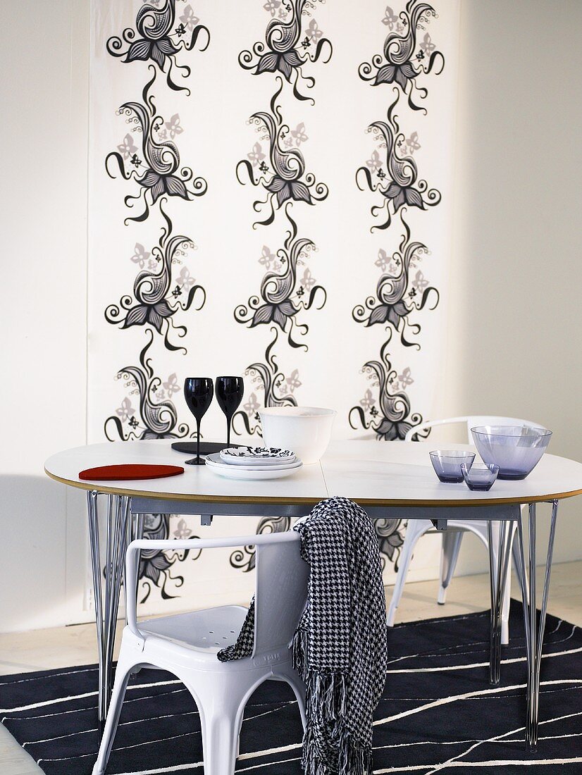 Stuhl und Esstisch mit Metallgestell vor Wandbehang mit schwarz weißem Ornamentmuster