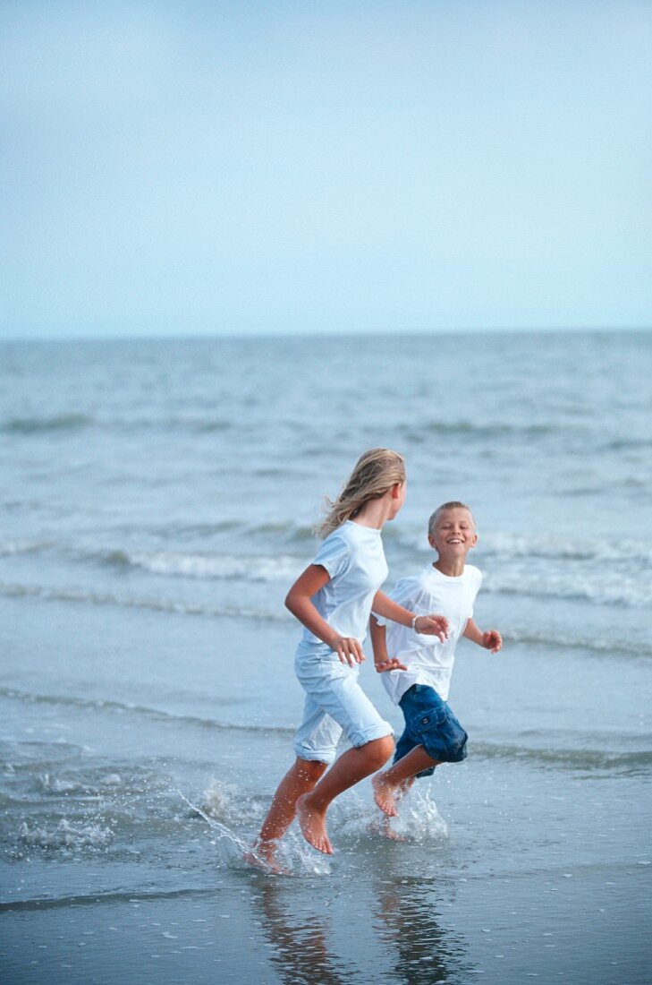 Mädchen und Junge laufen am Strand