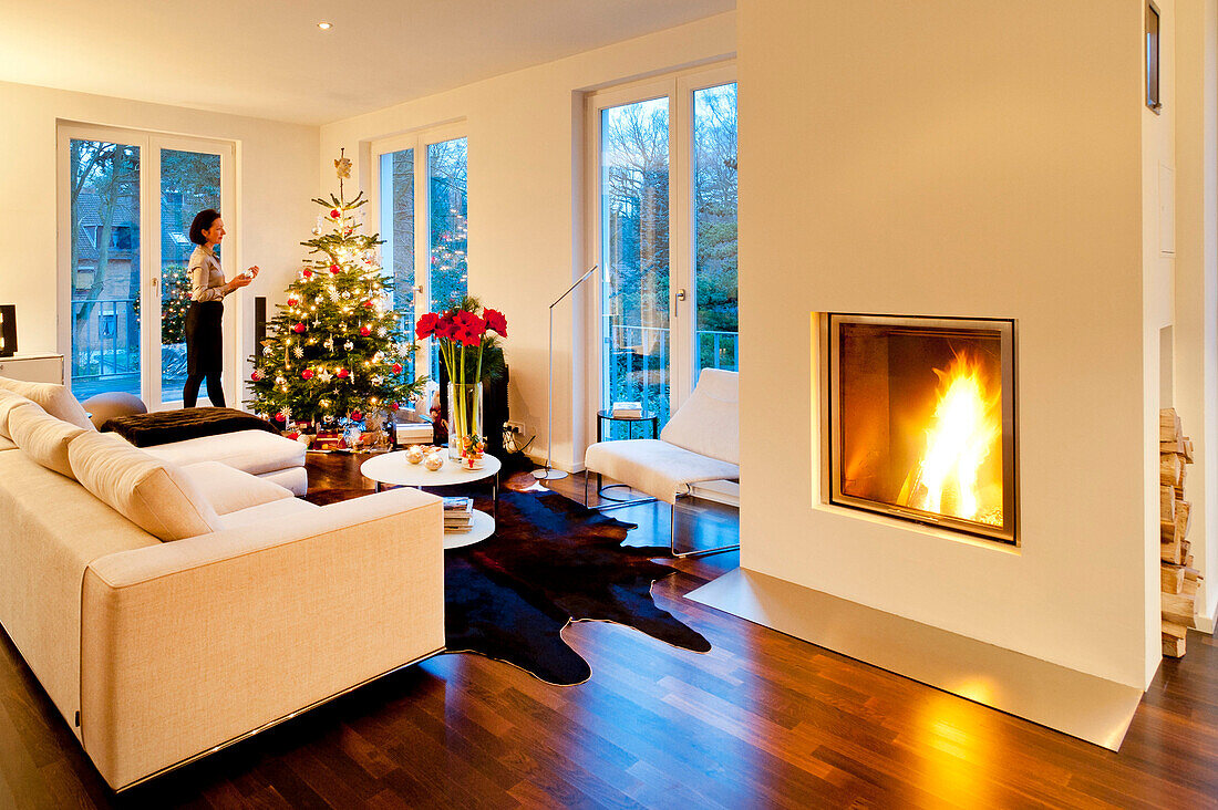 Modern flat with christmas tree and fireplace, Young woman dressing the tree, Hamburg, Germany