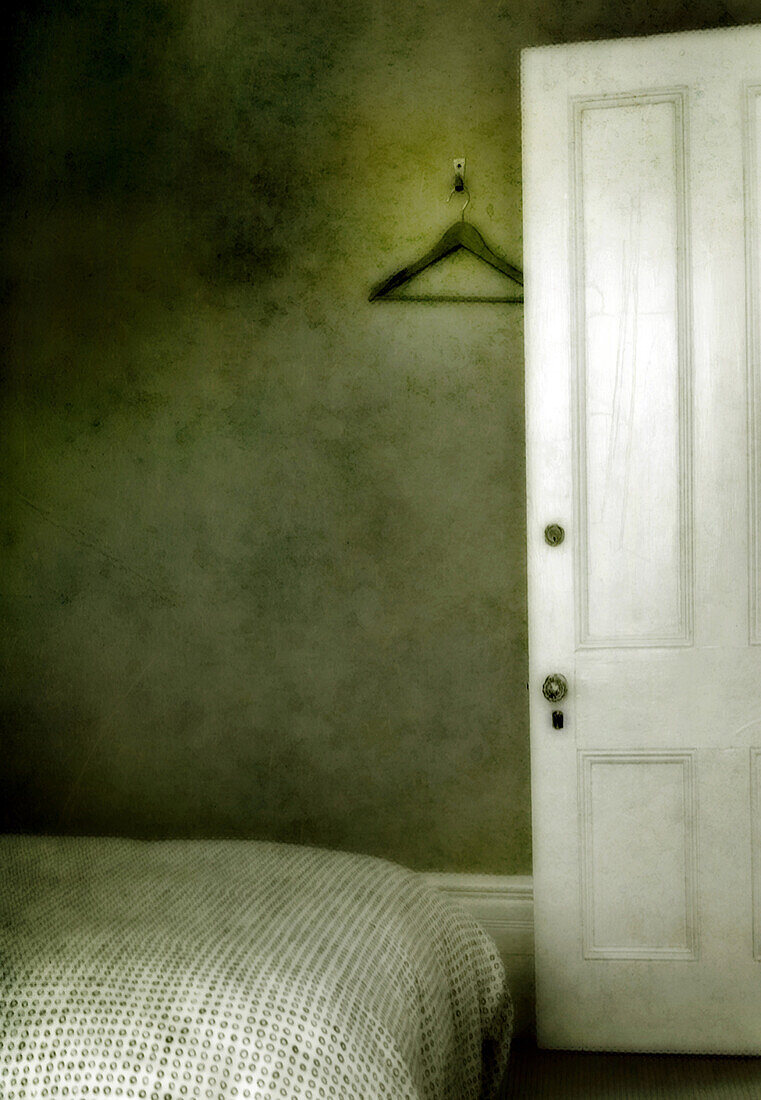 A traditionally furnished bedroom in an inn or small hotel in Gananoque, Ontario, Canada. Green wallpaper. A bed which is close to the open door. A hanger on a wall hook.