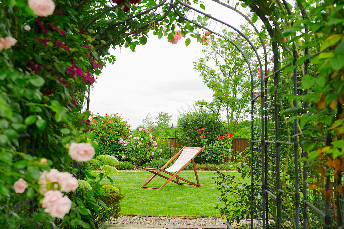 A country garden with a rose arch, and flowering climbing roses.