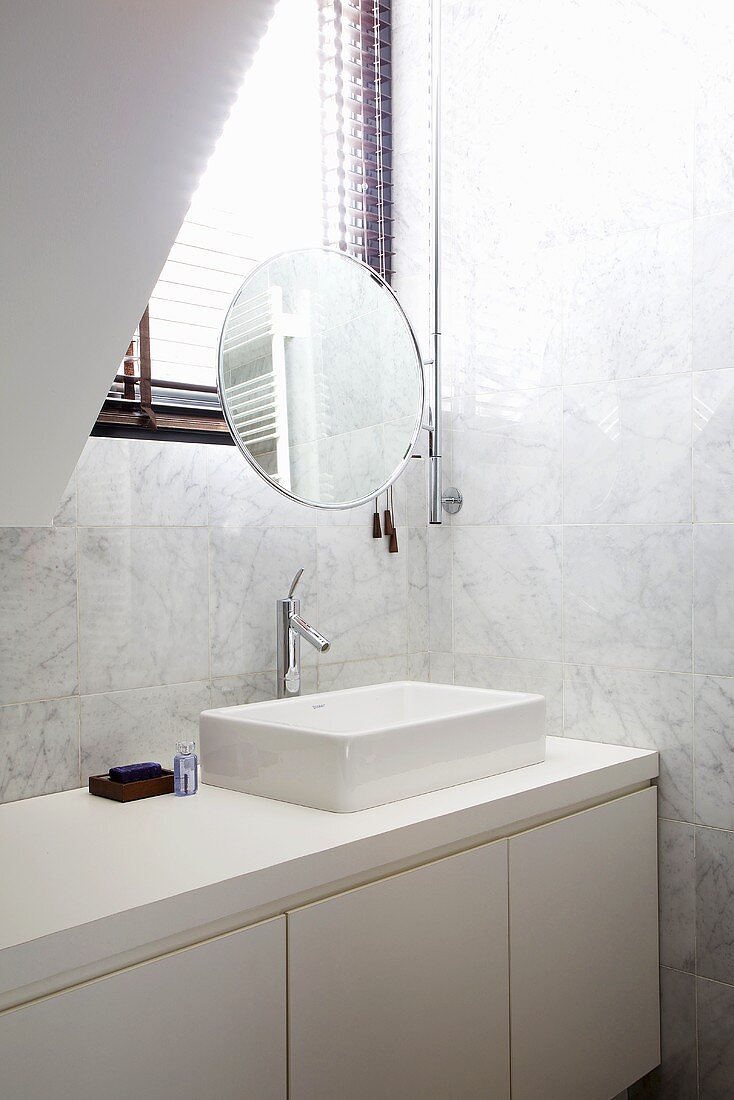White marble tiles and white built-in units in a bathroom with a make-up mirror at the window