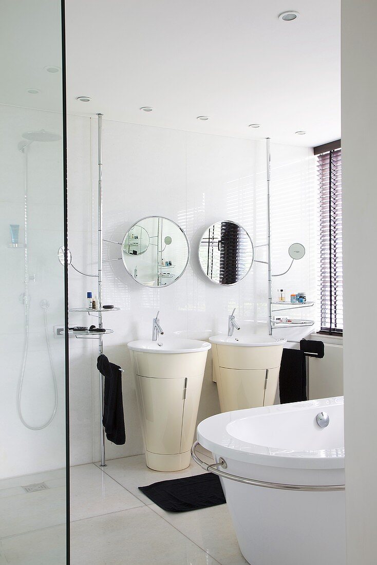 A white bathroom with a free-standing basin and a unit underneath it, a round mirror on the wall and black towels