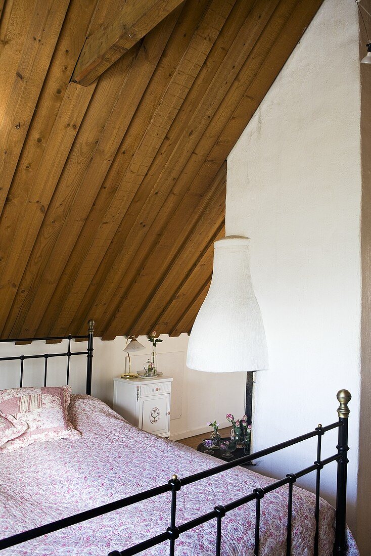 A metal bet under the slopping, wood panelled roof of an attic bedroom