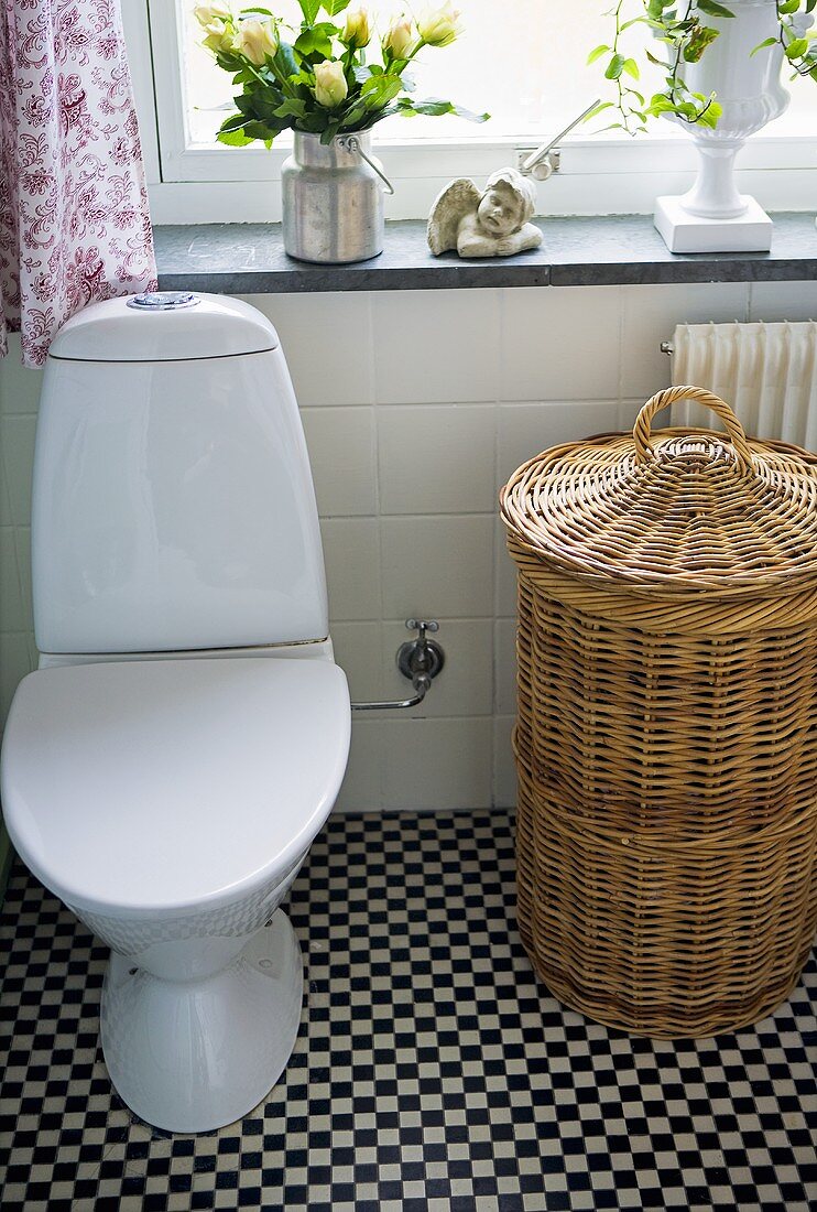A toilet and a wash basket in a bathroom with a chess board pattern