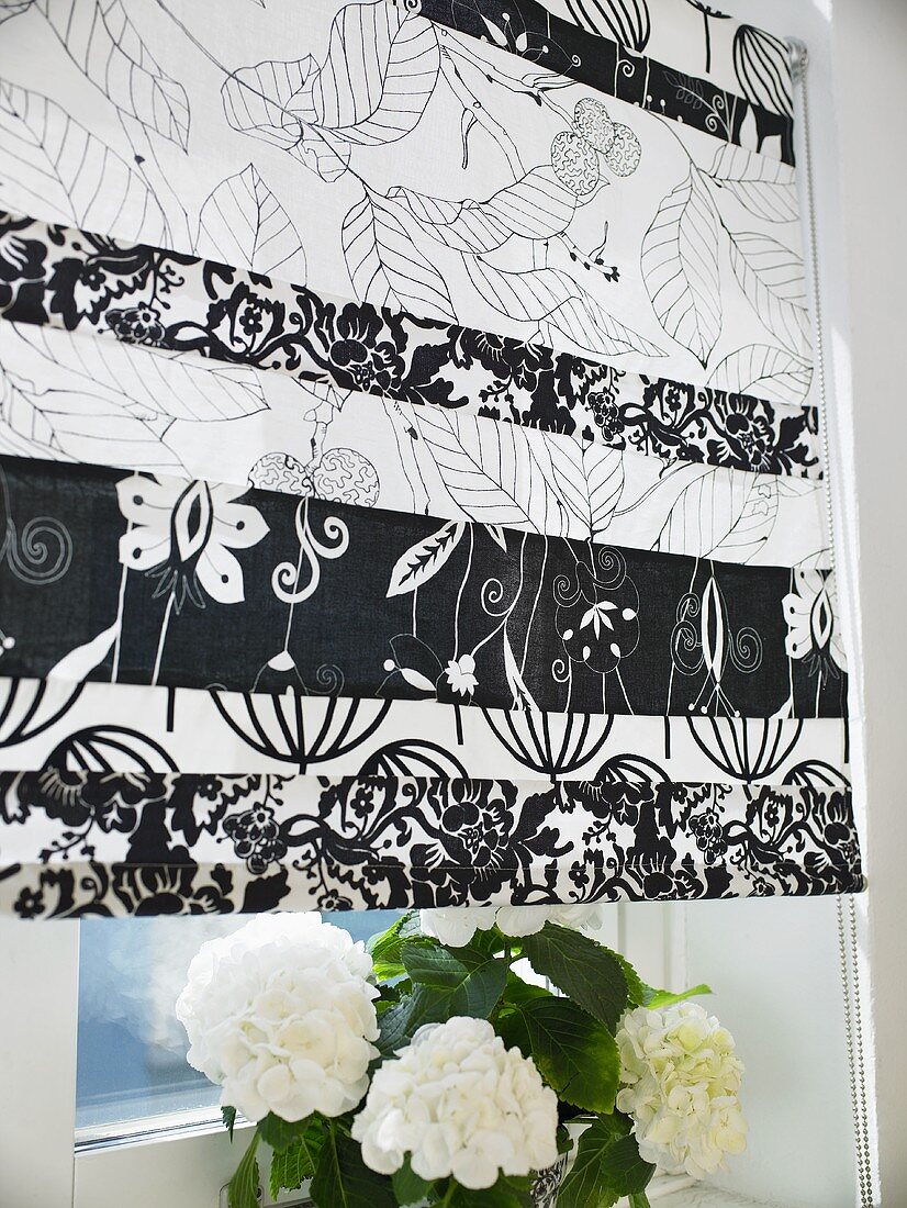 A black and white patterned blind and a flower pot on a window sill