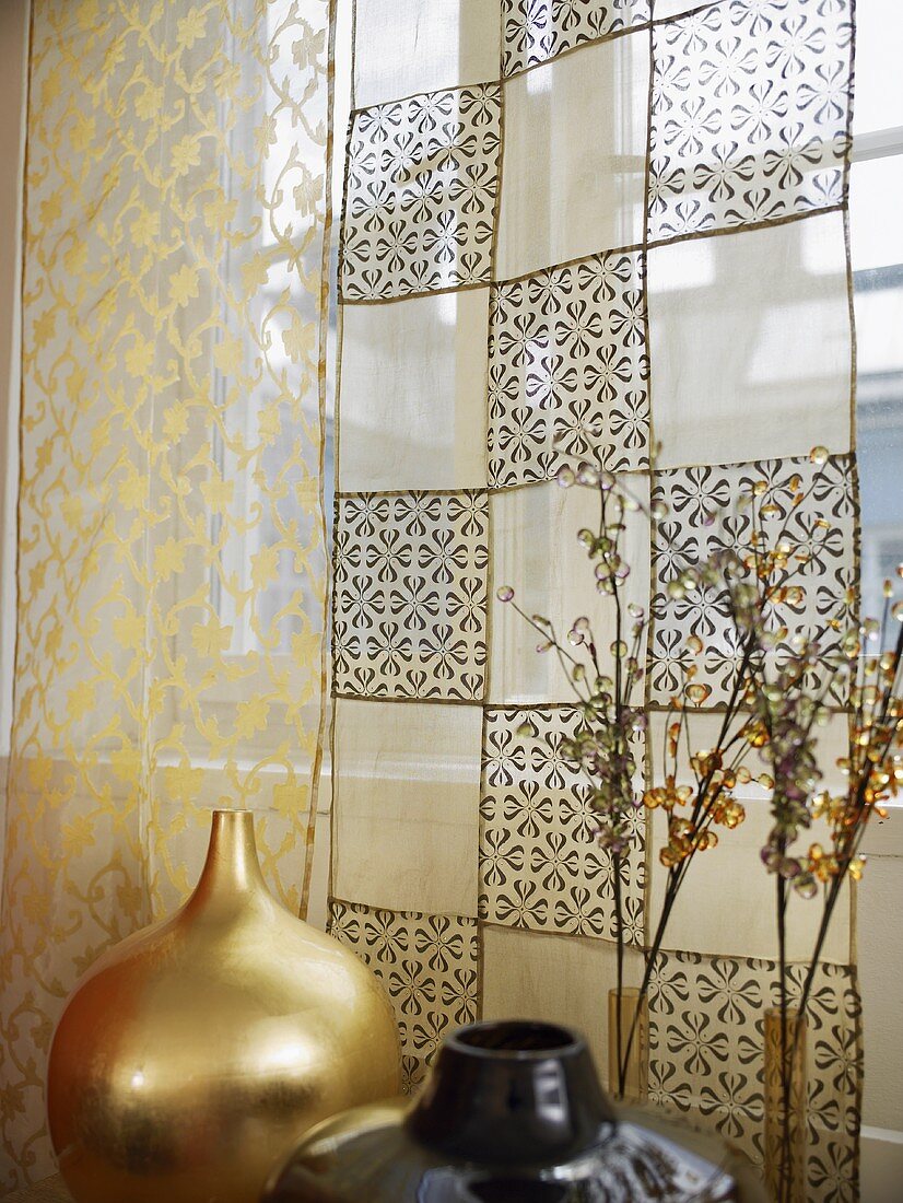A golden vase and a patterned, transparent curtain