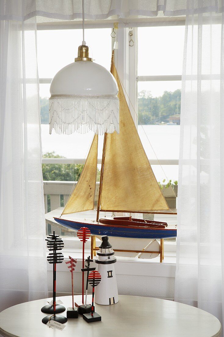 weiße Deckenlampe über Tisch am Fenster mit ausgestelltem Segelbootmodell