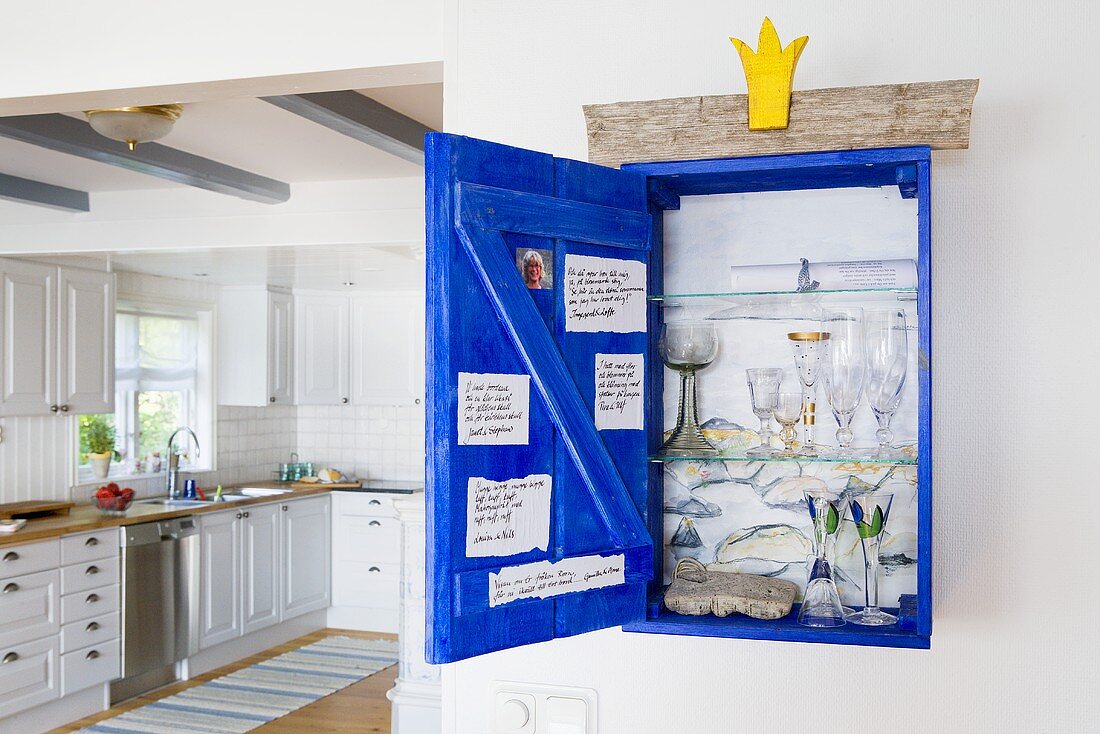Gläser im geöffneten Wandschränkchen und Blick in weiße Landhausküche