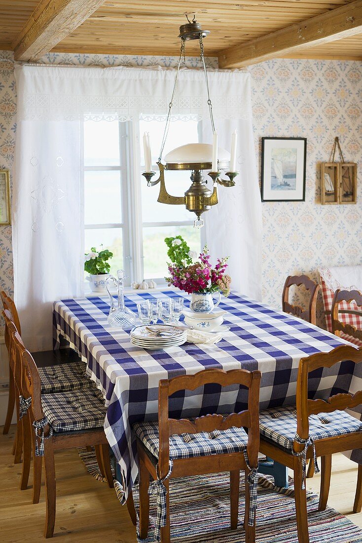 A cosy country dining room with a dining table with a checked table cloth in front of a window