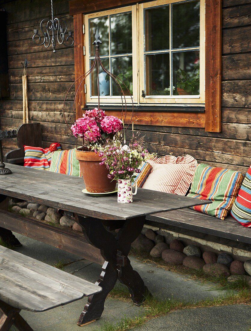 A rustic wooden table with colourful cushions against a wooden house facade