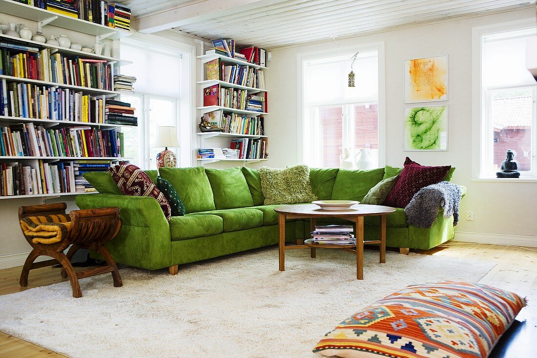 A corner of a living room with a green sofa and a book shelf next to a window