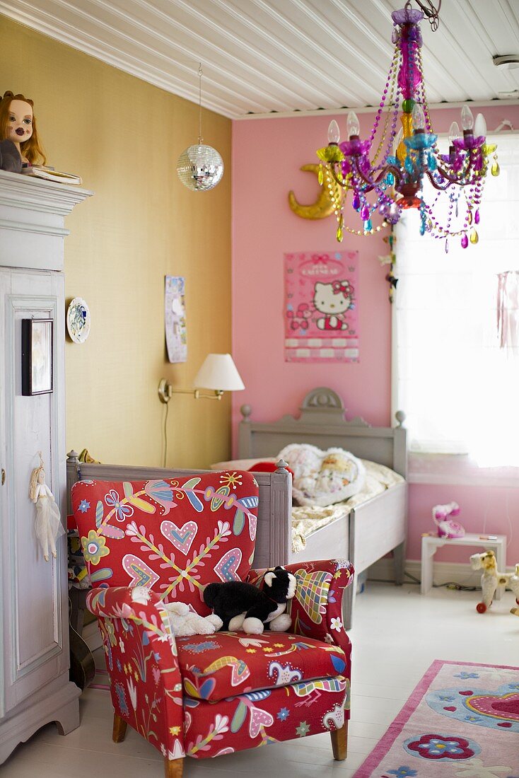 A child's room with a colourful reading chair in front of a bed and a chandelier hanging from the white wooden ceiling