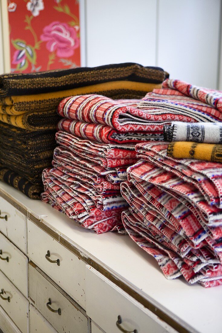 A stack of patterned blankets on a white, vintage chest of drawers