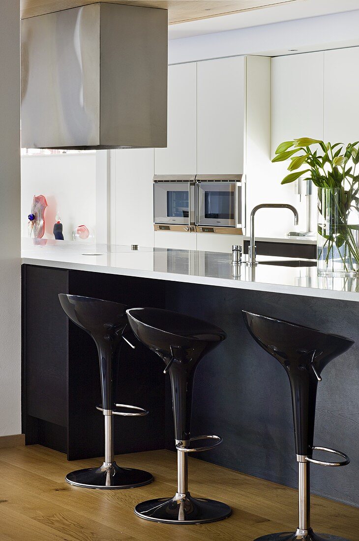 Black plastic bar stools in front of a kitchen counter with a white work surface