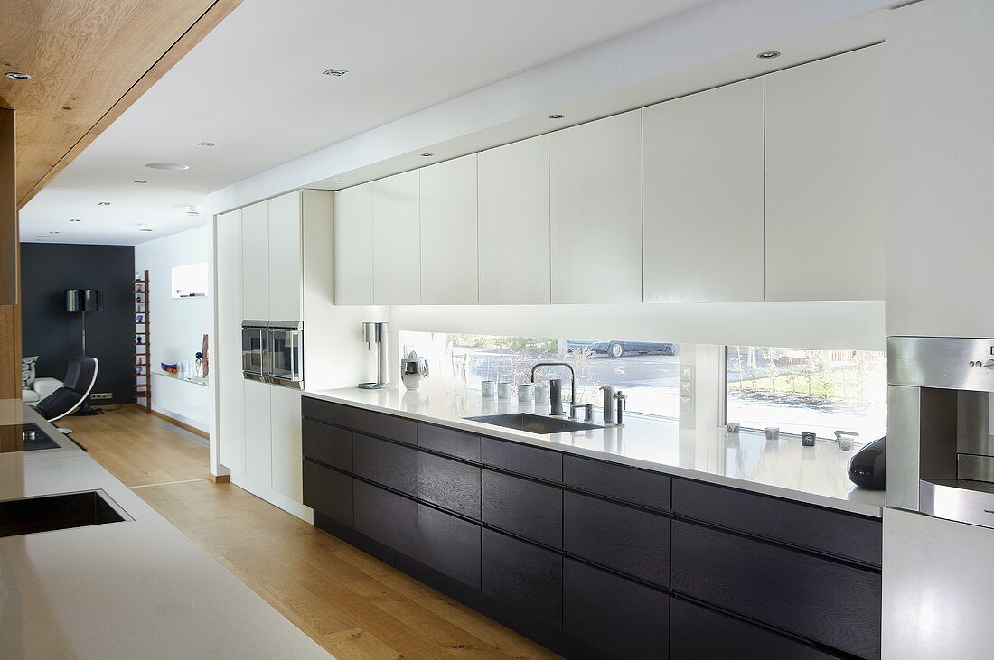 An open-plan designer kitchen - black and white fitted cupboards in front of a window bank