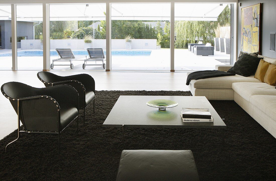 A living room room with a large window - black leather armchairs and a coffee table on a black rug with a view of the terrace